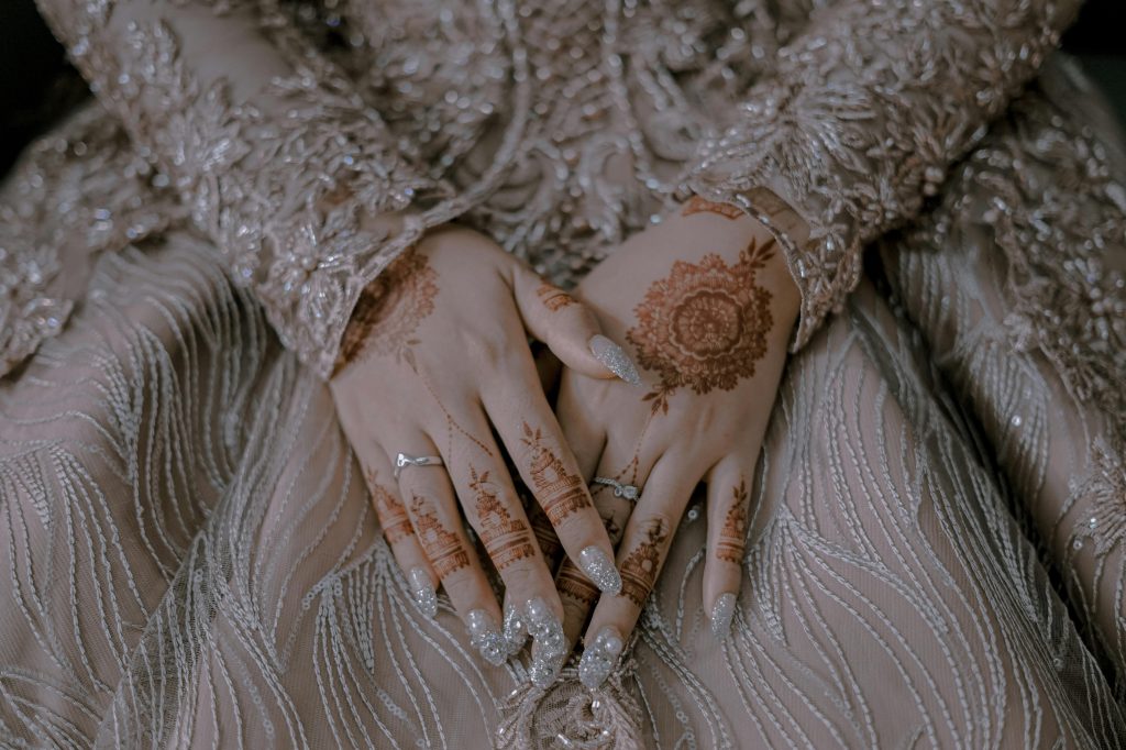 Close-up of a bride's hands adorned with henna and jewelry, showcasing intricate lace designs.
